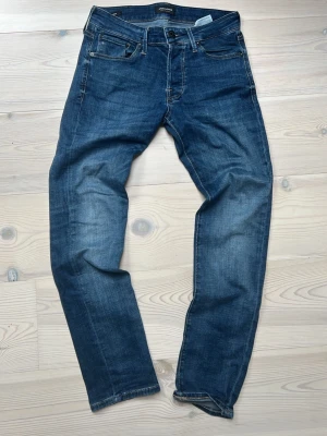 Mörkblå jeans från Jack & Jones - Säljer ett par klassiska mörkblå jeans från Jack & Jones med fem fickor och raka ben. Jeansen har snygga slitningar och kontrastsömmar, tillverkade i mjuk denim med lite stretch för extra komfort. Kontakta vid fler frågor eller bilder, kan gå ned i pris vid snabb affär 🤩