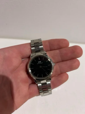 Daniel Wellington klocka - Stilren klocka från Daniel Wellington med svart urtavla och silverfärgat armband i rostfritt stål. Klassisk rund form och minimalistisk design utan siffror på urtavlan. Perfekt accessoar för dig som gillar enkel och tidlös stil.