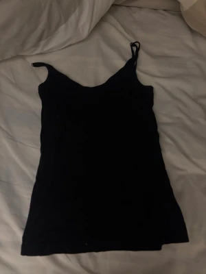 Svart linne med smala axelband - Ett enkelt svart linne med smala axelband och rak passform. Perfekt att styla lager på lager eller bära som det är. Linnet har en klassisk look och är ärmlöst, vilket gör det lättmatchat till olika outfits.