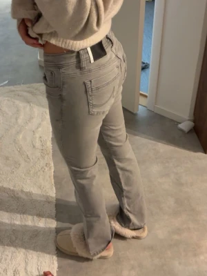 Grå bootcut jeans med låg midja - Säljer ett par gråa bootcut jeans med låg midja och klassiska fem fickor. Jeansen har en snygg tvätt och raka ben som går ut lite nedtill. Perfekta till sneakers eller boots och ger en avslappnad men trendig look.