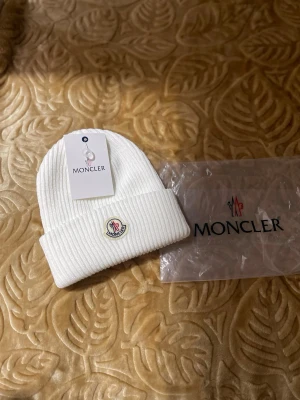 Vit ribbstickad mössa - Säljer en stilren vit ribbstickad mössa  med uppvikt kant och klassisk framtill. Mössan är tillverkad i mjukt material och passar perfekt för kalla dagar. Enkelt och snyggt plagg som lyfter din vinterstil.