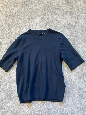 Mörkblå tröja från 157 - Mörkblå tröja från 157 med rund halsringning och halvlånga ärmar. Tröjan har ribbade muddar vid hals, ärmslut och nederkant. Enkel och stilren design som passar till många olika outfits.