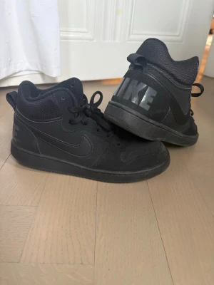 Svarta Nike high tops ungdom  - Helsvarta high top sneakers från Nike med stort NIKE-tryck på hälen. Bra höst/vinterskor pga färgen och stabilitet. Skorna har en mix av mocka och mesh. obs: det står 38 men 37 verkar vara mer sann. 