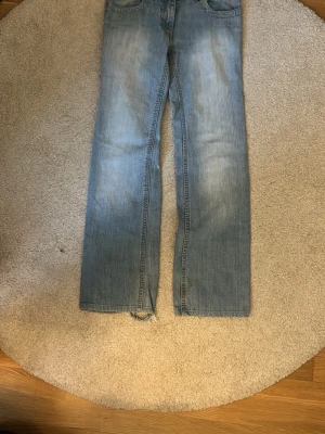 Ljusblå raka jeans - Säljer ett par ljusblå jeans med rak passform och slitningar vid bensluten. Jeansen har klassisk femficksdesign och är tillverkade i denim. Perfekta för en avslappnad och trendig look.