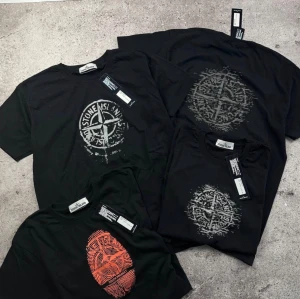 Svarta Stone Island t-shirts - (Finns i XS-S-M-L-XL) Fyra svarta t-shirts från Stone Island med olika tryck framtill, bland annat det klassiska kompassloggan i vitt och grått samt ett rött fingeravtryck. Alla har rund hals och korta ärmar. Perfekta för dig som gillar streetwear och vill ha något stilrent men ändå med edge.
