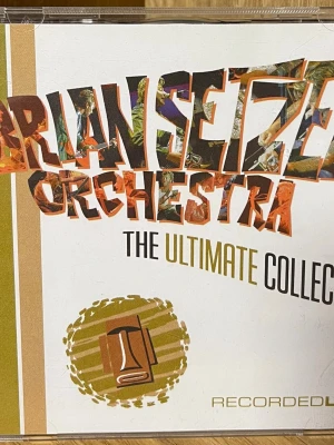 Brian Setzer Orchestra The Ultimate Collection - Säljer en CD med Brian Setzer Orchestra - The Ultimate Collection. Boxen innehåller två skivor med klassiska låtar och färgstark omslagsdesign med bilder på bandet och instrument. Perfekt för dig som gillar rockabilly och swing.