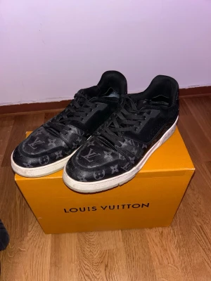 Louis Vuitton svarta monogram sneakers - Säljer ett par svarta Louis Vuitton sneakers med klassiskt monogrammönster över hela skon. Skorna har vita sulor och svarta skosnören. Materialet är en mix av läder och textil, och designen är chunky och modern med tydlig streetwear-vibe.