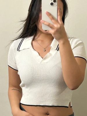 Vit ribbad croppad polotopp H&M - Vit ribbad croppad polotopp från H&M med svarta detaljer på krage och ärmslut. Toppen har korta ärmar, v-ringning och en klassisk pikékrage. 