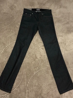Mörkblå raka jeans från Filippa K - Snygga mörkblå jeans från Filippa K med klassisk rak passform och fem fickor. Jeansen är tillverkade i ett robust denimtyg och har stilrena detaljer med silverfärgade nitar. Perfekta för en clean och tidlös look.