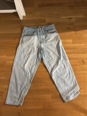 Ljusblåa baggy jeans från EMPYRE - Säljer ett par ljusblåa baggy jeans från EMPYER med broderad logga på bakfickorna. Jeansen har en avslappnad passform, klassisk femficksdesign och är tillverkade i denim. Perfekta för en streetwear-look.