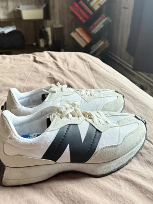 Vita New Balance sneakers med svart N - Snygga vita sneakers från New Balance med stor svart N-logga på sidan. Skorna har en chunky sula, ovandel i mesh och mocka samt vita skosnören. Perfekta för dig som gillar en clean och sportig look. 