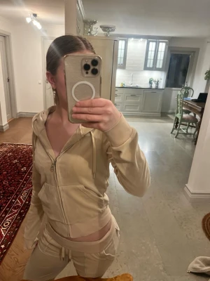 Juicy couture zip hoodie - Säljer ett beige loungewear-set från Juicy Couture i mjuk velour. Setet består av en zip-hoodie med fickor, dragsko i huvan och broderad logga på bröstet samt matchande byxor med resår och snörning i midjan. Perfekt för en chill och trendig vibe.😊