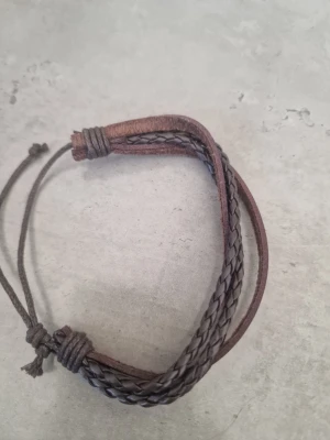 Brunt justerbart läderarmband - Snyggt armband i brunt läder med både släta och flätade band. Justerbar storlek med dragsko som gör det enkelt att ta på och av. Perfekt accessoar för en avslappnad och trendig stil. Passar både tjejer och killar.
