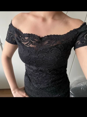 Svart spetsklänning offshoulder - Säljer en svart, figurnära klänning med offshoulder och korta ärmar. Klänningen är täckt av vacker spets och har en feminin, elegant look. Perfekt för dig som gillar detaljer och en stilren känsla.