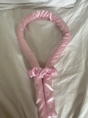 Rosa satin värmerulle för håret - Säljer en ljusrosa värmerulle i satinmaterial, perfekt för att skapa lockar utan värme. Mjuk och flexibel design som är enkel att använda och bekväm att sova med. Kommer med matchande scrunchies för att hålla håret på plats.