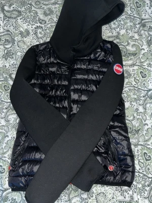 Svart pufferjacka från Colmar BYTE GÅR OCKSÅ - Säljer en svart pufferjacka från Colmar Originals med huva och vadderade paneler. Jackan har svarta ärmar i mjukt material och klassisk Colmar-logga på ena ärmen. Perfekt för kalla vinterdagar och riktigt snygg streetstil.