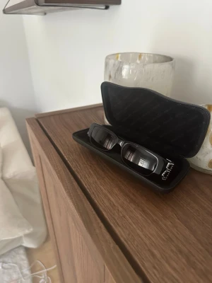 Balenciaga solglasögon - Snygga svarta solglasögon med rektangulära bågar. Kommer i ett stilrent svart etui. Perfekta för dig som gillar en clean och modern look. Passar till de flesta outfits och ger en cool vibe. Stilrena och exklusiva solglasögon från balenciaga. Nypris 5200