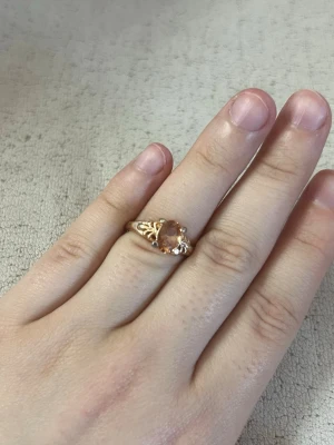 Guldfärgad ring med orange sten - Snygg guldfärgad ring med en oval orange sten i mitten. Ringen har detaljerade utskärningar på sidorna som ger en vintagekänsla. Perfekt accessoar för dig som vill sticka ut lite extra.