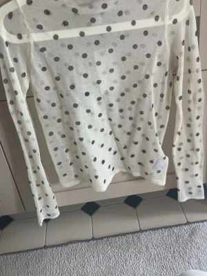 Vit prickig mesh polotopp - Säljer en transparent vit mesh polotopp med svarta prickar. Toppen har lång ärm och är figurnära i modellen, perfekt för att styla lager på lager. Supersnygg till både jeans och kjol! skriv för fler bilder!