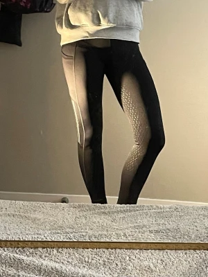 Ridbyxor  - Ett par svarta ridbyxor med lite reflexer på sidorna vid knät och med två fickor på sidorna 