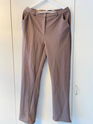 Beige kostymbyxor från 157 - Snygga beige kostymbyxor från 157 med raka ben och klassisk passform. Byxorna har hällor för skärp, knapp och dragkedja framtill samt sidofickor. Perfekta för en clean och stilren look.