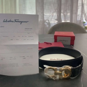 Svart bälte från Salvatore Ferragamo - Stilrent svart bälte från Salvatore Ferragamo med exklusivt guldfärgat spänne i metall. Klassisk design som passar till många olika looks. Levereras med originalförpackning och påse.