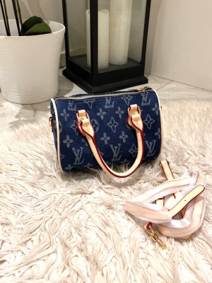 Denim handväska  - Säljer en snygg blå handväska i denim med klassiskt mönster. Väskan har ljusa läderhandtag och detaljer samt medföljande axelrem. Perfekt för dig som gillar lyxiga accessoarer med unik stil.