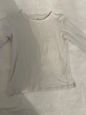 Vit långärmad topp från H&M - En enkel och stilren vit långärmad topp från H&M. Tillverkad i mjuk bomull med rund halsringning och normal passform. Perfekt basplagg att matcha med allt i garderoben.
