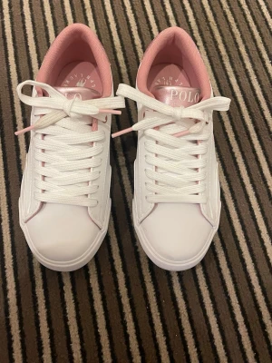 Vita och rosa sneakers från Polo Ralph Lauren - Säljer mina snygga vita sneakers från Polo Ralph Lauren i stl 39 med rosa detaljer på insidan och logga på plösen. Endast använda en gång men för små för mig. Skorna har klassisk låg profil, vita snören.Perfekta stilrena sneakers nu till våren. Köpt från Zalsndo nypris 979 kr