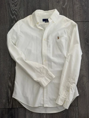  Ralph Lauren Skjorta Slim Fit - Klassisk vit skjorta från Ralph Lauren i slim fit-modell storlek M, har används ett fåtal gånger. Den är Tillverkat i mjukt bomull och passar perfekt till en clean och stilren look. Hör av dig vid intresse!