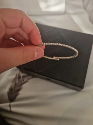 Glittrigt silverfärgat armband - Ett stilrent armband i silverfärg med gnistrande stenar runt hela bandet. Armbandet är tunt och har en rund form, perfekt för att ge en extra touch till din outfit. Materialet ser ut att vara metall med infattade små stenar som ger ett lyxigt intryck.