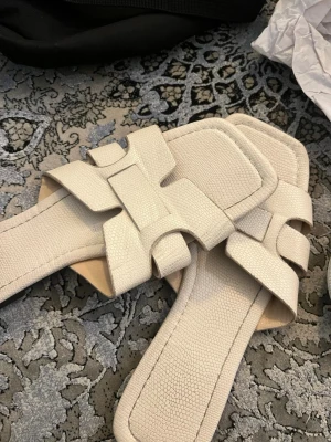 Beige sandaler med breda remmar - Stilrena beige sandaler med breda korslagda remmar och fyrkantig tå. Tillverkade i ett strukturerat material som liknar läder. Sulan är svart och har bra grepp. Perfekta för en avslappnad och trendig look.