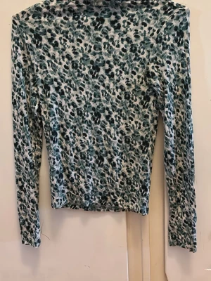 Leopardmönstrad långärmad topp Stradivarius - Säljer en långärmad topp från Stradivarius med leopardmönster i gröna och svarta toner på vit botten. Toppen har en figurnära passform och är tillverkad i mjuk, stretchig polyester. Perfekt för dig som vill sticka ut lite extra.