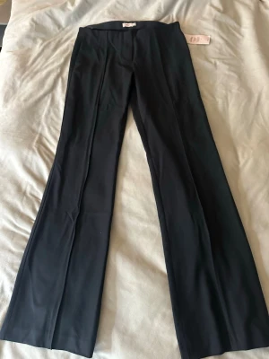 Svarta kostymbyxor från Nelly - Stilrena svarta kostymbyxor från Nelly med raka ben och pressveck. Byxorna är låg midjade och är tillverkade i ett mjukt, vävt material som ger en snygg siluett. Perfekta för en dressad look. Inte använde någon gång så dem är som nya. 