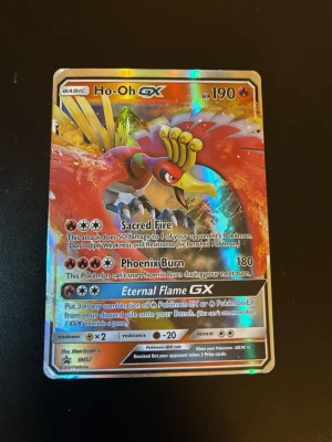 Pokémonkort Ho-Oh GX holografisk - Säljer ett Pokémonkort med Ho-Oh GX motiv. Kortet är holografiskt och har färger i rött, gult och orange med metallic-effekt. Det är en samlarkort från Pokémon TCG och har attacker som Sacred Fire, Phoenix Burn och Eternal Flame GX.