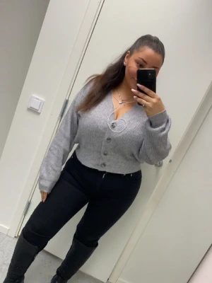 Grå ribbstickad kofta med knappar - Grå ribbstickad kofta med v-ringning och stora knappar framtill. Modellen är croppad och har långa ärmar med breda muddar.