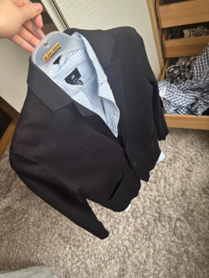 Svart kavaj från cos - Stilren svart kavaj från COS med klassisk passform och två knappar framtill. Kavajen har spetsiga slag och två framfickor. Perfekt för dig som vill ha en enkel och snygg look. Materialet ser ut att vara en blandning av polyester och viskos.