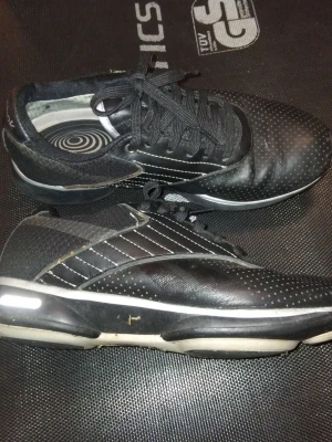 Svarta Reebok sneakers med vita detaljer - Snygga svarta sneakers från Reebok med vita prickar och vita detaljer på sulan. Skorna har snörning, lågt skaft och en modern design med både läder och textilmaterial. Perfekta för dig som gillar en stilren och sportig look.