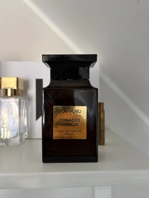 Tom Ford Tobacco Vanille EdP 100ml - Tom Ford Tobacco Vanille Eau de Parfum i en elegant mörkbrun glasflaska med guldlabel. Flaskan har en fyrkantig form och rymmer 100 ml. Doften är känd för sina varma toner av tobak och vanilj, vilket ger en lyxig och sofistikerad känsla.