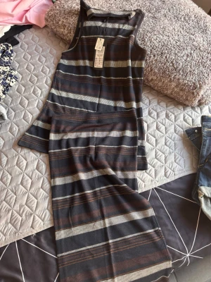 Randig långklänning från Monki - Säljer en lång, ärmlös set top och peny kjol från only med horisontella ränder i mörkblått, brunt och beige.  har en rund halsringning och är gjord i mjuk, stickad bomull. Perfekt för dig som gillar en avslappnad men ändå stilren look.