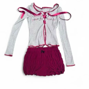 Grå och vinröd pyjamas med rosetter - Söt pyjamas med långärmad grå topp och vinröda detaljer, dekorerad med rosetter och texten 'i know i'm your favorite' framtill. Matchande vinröda shorts med volang och liten rosett. Ribbat material, perfekt för mysiga kvällar.