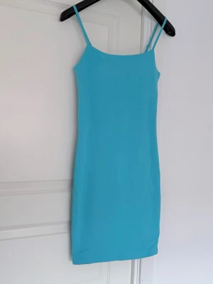 Turkos kort klänning med smala band - En enkel och stilren turkos klänning från H&M med smala axelband och rak passform. Klänningen är kort och har en mjuk, stretchig känsla som gör den bekväm att bära. Perfekt för varma dagar eller sommarens alla tillfällen.