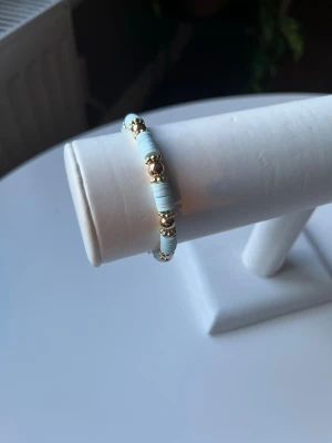  Blått somrigt armband med guldiga detaljer  -  Ett blått somrigt armband med guldiga detaljer. Elastiskt band så att det är lätt att ta på och av det är även handgjort.