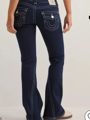 Mörkblå bootcut jeans True Religion - Säljer ett par mörkblå bootcut jeans från True Religion med kontrasterande vita sömmar och ikoniska fickdetaljer bak. Jeansen har låg midja, knappgylf och är tillverkade i stretchig denim för skön passform. Perfekta för dig som gillar en klassisk men trendig look. Jeansen är endast testade! Storlek 25, jag är 165 de är lite långa på mej ❤️❤️kommer ej gå ner i pris 
