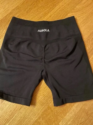 Svarta träningstights från Aurola - Säljer ett par svarta, högmidjade träningstights från Aurola. De har en tight passform och är tillverkade i ett stretchigt syntetmaterial som passar perfekt för gym eller annan träning. Klassisk design utan mönster och med diskret logga i midjan.