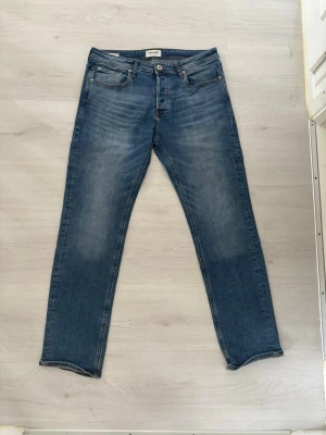 Blå jeans från Jack & Jones - Snygga blå jeans från Jack & Jones med klassisk femficksdesign och raka ben. Jeansen har en lätt tvättad look och är tillverkade i bomull med en bekväm passform. Perfekta för en avslappnad stil.