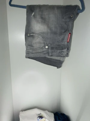 Grå Dsquared2 Keel jeans - Säljer ett par grå jeans från Dsquared2, modell Keel. Jeansen har en snygg tvätt med slitningar och klassiska fem fickor. Röd Dsquared2-tag vid fickan och läderpatch bak i midjan. Perfekta för dig som vill ha en trendig och avslappnad look.