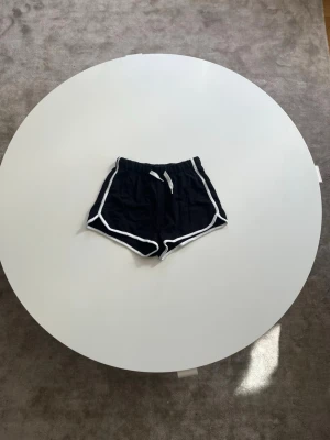 Svarta shorts med vit kant - Säljer ett par svarta shorts med vit kant och snörning i midjan. Shortsen har elastisk midja och är tillverkade i mjukt material för maximal komfort. De är gjorda i storlek 146 från H&M.🥰