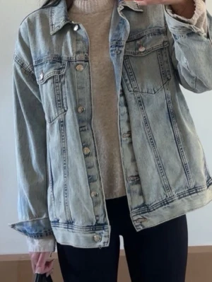Oversized ljusblå jeansjacka - Säljer en oversized ljusblå jeansjacka med klassisk krage, bröstfickor med lock och silverfärgade knappar. Jackan har en avslappnad passform och är tillverkad i denim. Perfekt att slänga över en hoodie eller tröja för en cool look. (Bud) 