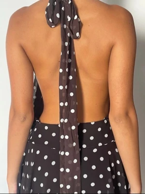 Prickig halterneck klänning - Snygg klänning med vita prickar och öppen rygg. Halterneck-modell som knyts i nacken och har ett flowy, luftigt tyg. Perfekt för dig som vill ha en trendig och bekväm look med lite extra edge. Kort modell som passar till varma dagar.